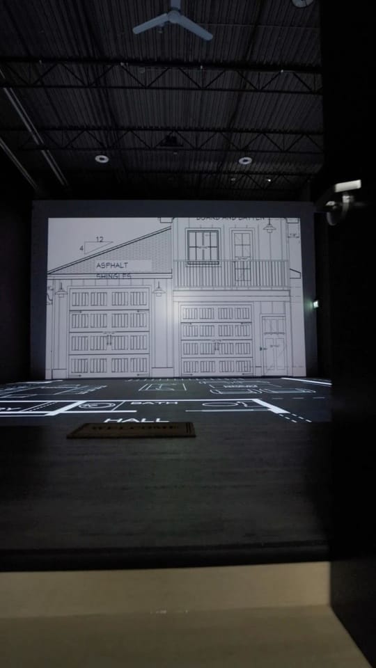 A house elevation lit on the studio's wall-size screen above a floor plan on the LED floor